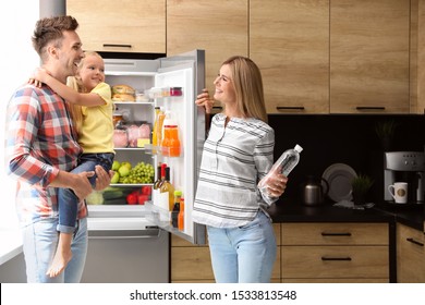 Happy Family With Bottle Of Water Near Refrigerator In Kitchen