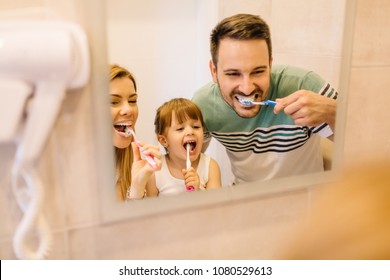 Happy Family Is Brushing Their Teeth In Front Of The Mirror In Bathroom