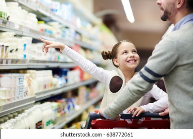 Happy Family Buying Groceries: Smiling Little Girl Choosing Dairy Products From Fridge In Milk Aisle While Shopping In Supermarket