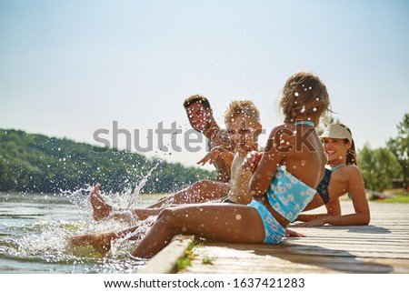Happy family by the lake in summer holding feet in water