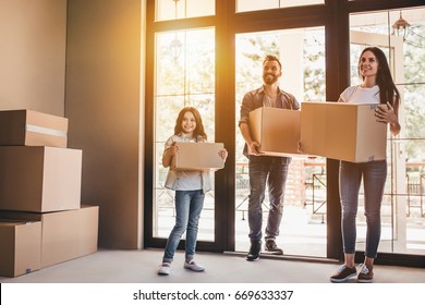 Happy Family With Cardboard Boxes In New House At Moving Day.