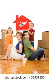 Happy Family With Cardboard Boxes In Their New Home Showing The House Sold Sign - Isolated