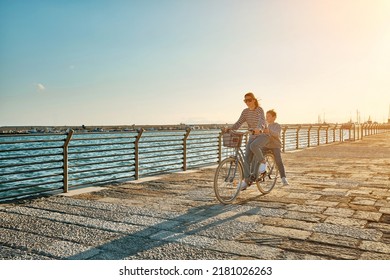 Happy Family, Carefree Mother And Son With Bike Riding On Beach Having Fun, On The Seaside Promenade On A Summer Day, Enjoying Vacation. Togetherness Friendly Concept