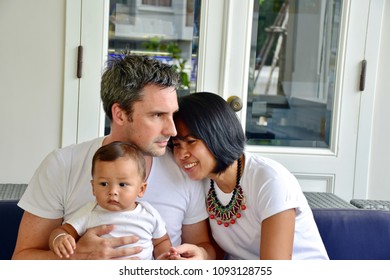 Happy Family, Caucasian Man And Asian Woman, Mom And Dad With Son Is Mix Race, Happiness Of All Sit On Blue Sofa In Living Room At Home Decorate In Contemporary Style, Diversity Culture Concept   