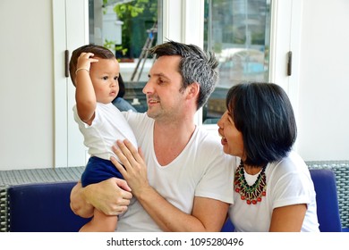 Happy Family, Caucasian Man And Asian Woman, Mom And Dad With Son Is Mix Race, Happiness Of All Sit On Blue Sofa In Living Room At Home Decorate In Contemporary Style, Diversity Culture Concept 