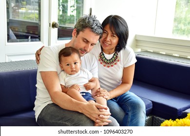 Happy Family, Caucasian Man And Asian Woman, Mother And Father With Son Is Mix Race, Happiness Of All Sit On Blue Sofa In Living Room At Home Decorate In Contemporary Style, Diversity Culture Concept 