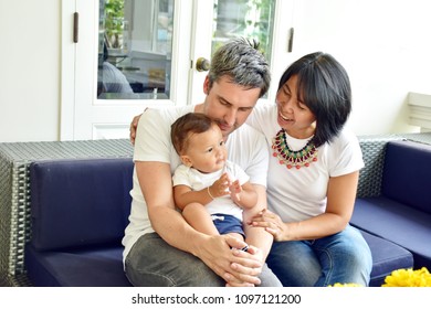 Happy Family, Caucasian Man And Asian Woman, Mother And Father With Son Is Mix Race, Happiness Of All Sit On Blue Sofa In Living Room At Home Decorate In Contemporary Style, Diversity Culture Concept 