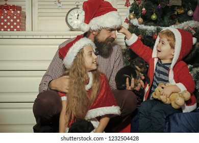 Happy Family Celebrate New Year And Christmas. Father And Child With Puppy. Father And Children In Santa Hat At Christmas Tree. Winter Holiday And New Year Of Dog. Xmas Party Celebration.