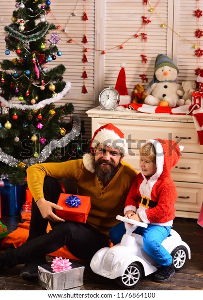 Happy family celebrate new year and Christmas.\
Father and child on car with new year present box. Xmas party\
celebration. Father and son in santa hat at Christmas tree. Winter\
holiday and boxing day.