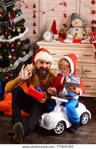Happy family celebrate new year and\
Christmas. Father and child on car with new year present box.\
Winter holiday and boxing day. Father and son in santa hat at\
Christmas tree. Xmas party\
celebration.