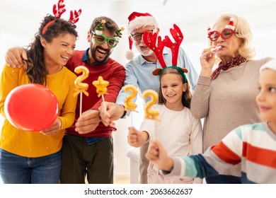 Happy Family Celebrating Christmas At Home, Having Fun Holding Balloons Shaped As Numbers 2022, Representing The Upcoming New Year