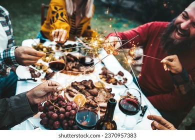Happy family celebrating with fireworks at barbecue backyard party - Young people having fun with fire sparklers at night time - Friends drinking red wine at farmhouse restaurant - Youth concept