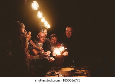 Happy Family Celebrating Holidays With Sparklers Fireworks At Night Dinner Party - Group Of People With Different Ages And Ethnicity Having Fun Together