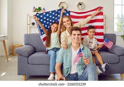 Happy family celebrating Independence Day at home. Portrait of happy young American family with children who are holding national flags. Family is sitting on sofa at home and smiling at camera. - Powered by Shutterstock