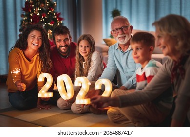 Happy Family Celebrating New Years Eve At Home With Kids, Sitting By The Christmas Tree, Holding Sparklers And Illuminative Numbers 2022 Representing The Upcoming New Year