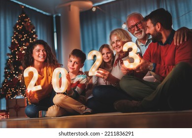 Happy family celebrating New Years Eve at home with kids, sitting by the Christmas tree, holding sparklers and illuminative numbers 2023 representing the upcoming New Year - Shutterstock ID 2211836291