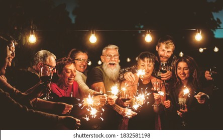 Happy family celebrating with sparklers fireworks at night party - Group of people with different ages and ethnicity having fun together - Holidays lifestyle concept