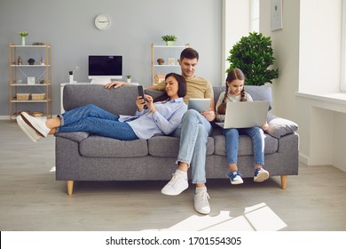 Happy Family Chatting Online Using Laptop While Sitting With Baby On Sofa At Home.