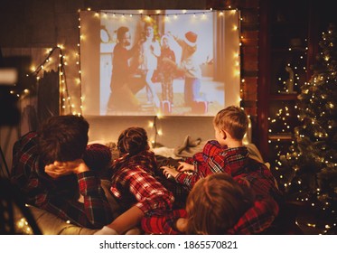happy family in checkered pajamas: mother father and children watching projector, TV, movies with popcorn in christmas holiday evening   at home 
