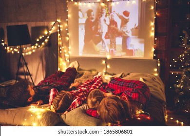 happy family in checkered pajamas: mother father and children watching projector, TV, movies with popcorn in christmas holiday evening   at home 
 - Powered by Shutterstock