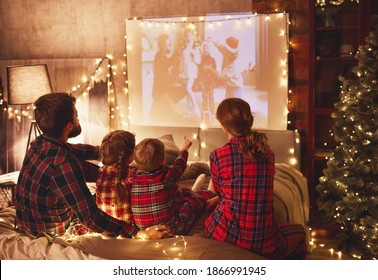 Happy Family In Checkered Pajamas: Mother Father And Children Watching Projector, Film, Movies With Popcorn In Christmas Holiday Evening   At Home 
