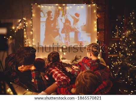 happy family in checkered pajamas: mother father and children watching projector, TV, movies with popcorn in christmas holiday evening   at home 
