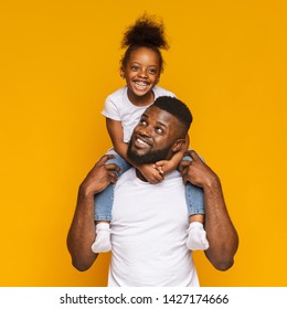 Happy Family. Cheerful Black Man Riding His Cute Little Daughter On Shoulders, Orange Studio Background