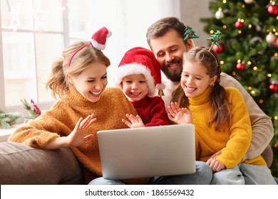 Happy Family Cheerful Parents And Joyful Children Make A Video Call To Relatives On  Holiday Near The Christmas Tree At Home
