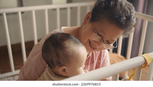 Happy Family cheerful Senior Asian woman grandmother holding playing with cute little baby toddler granddaughter smile laugh together and hugging with love while sitting indoors room at home - Powered by Shutterstock