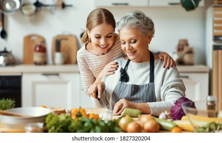 Happy Family Cheerful Young Woman Embracing Mature Mother While Preparing Healthy Dish With Fresh Vegetables In Home Kitchen
