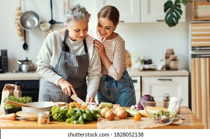 Happy Family Cheerful Young Woman Embracing Mature Mother While Preparing Healthy Dish With Fresh Vegetables In Home Kitchen
