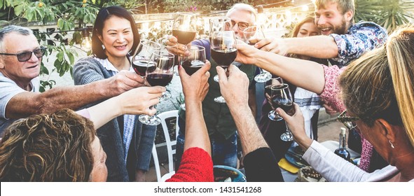 Happy family cheering with red wine at barbecue dinner outdoor - Different age of people having fun at sunday meal - Food, taste and summer concept - Soft focus on close-up hands