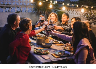 Happy family cheering with red wine at barbecue dinner outdoor - Different age of people having fun at weekend meal - Food, taste and summer concept - Main focus on left hands toasting