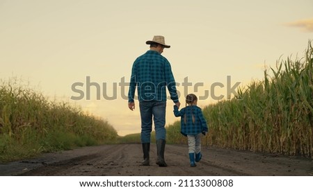Happy family, child father walk together hand in hand on plantation in autumn. Farmer father works in cornfield with his little daughter. Family business of farmers. Dad daughter looks at corn harvest