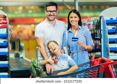 Happy Family With Child And Shopping Cart Buying Food At Grocery Store Or Supermarket, Woman Holding Credit Card.