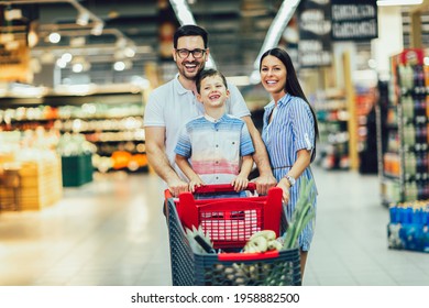 Happy family with child and shopping cart buying food at grocery store or supermarket - Shutterstock ID 1958882500