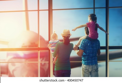 Happy Family With Children At The Airport. Parents And Their Children Look Out The Window At The Plane.