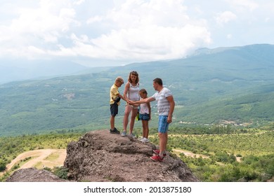 Happy Family With Children Holding Hands Stands On Rocks On Hill. Concept Of Family Trip In Mountains. Father, Mother, Daughter And Son Have Fun In Nature