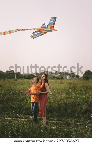 Happy family and children run on meadow with a kite in the summer on the nature. Family playing with kite while running along rural summer field. Family day