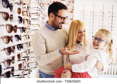 Happy family choosing glasses in optics store. 