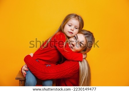 Happy family in Christmas red knit jumpers hugging on yellow studio background. Merry Christmas