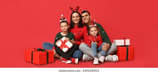 Happy family in Christmas sweaters and with gifts on red background 