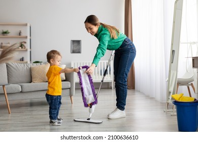 Happy family cleaning the room. Mother and toddler son doing the cleaning at home, little kid boy helping mom washing floor in living room, giving her rug