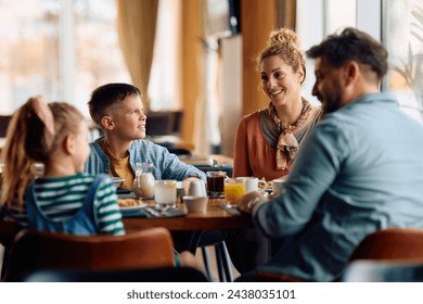 Happy family communicating while eating breakfast at dining table in hotel restaurant. Focus is on woman. - Powered by Shutterstock