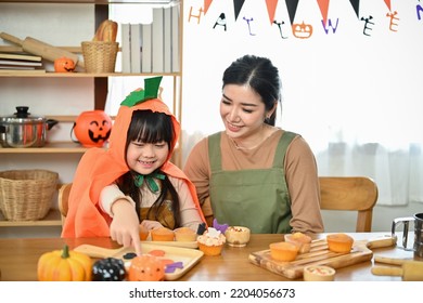 Happy Family Concept, An Adorable Little Asian Girl Enjoys Making And Decorating Halloween Cupcakes With Her Mom In The Kitchen.