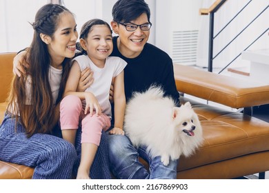 Happy Family Concept Asian Father And Mother And Six Year Old Daughter Sitting On The Sofa With The Little White Dog Watching TV Together Happily In The Living Room Of The House.