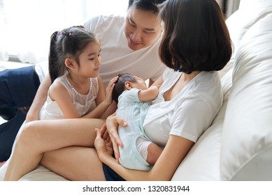 Happy family concept. Breast feeding newborn baby at home. The father and big sister stay close to mother and baby and looking at them, embracing and supporting her and the baby. 