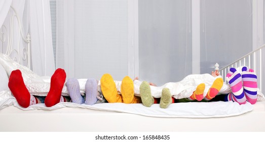 Happy family concept. Feet of father, mother and four children in colorful knitted socks on white bed. Family sleeping together.