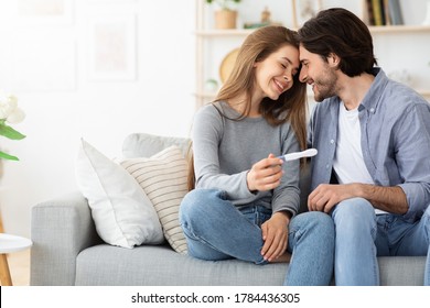 Happy family concept. Married couple bonding on couch and holding positive pregnancy test, home interior, free space
