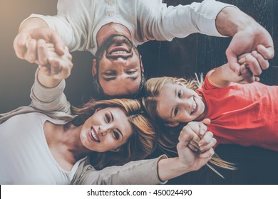 Happy Family Concept. Top View Of Happy Family Of Three Bonding To Each Other And Smiling While Lying On The Hardwood Floor